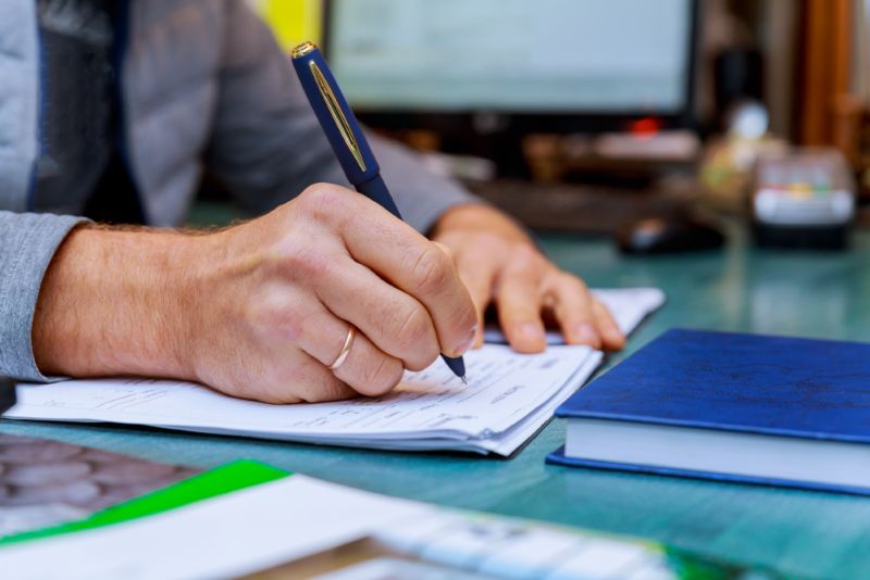 Man wearing a wedding ring signing a piece of paper