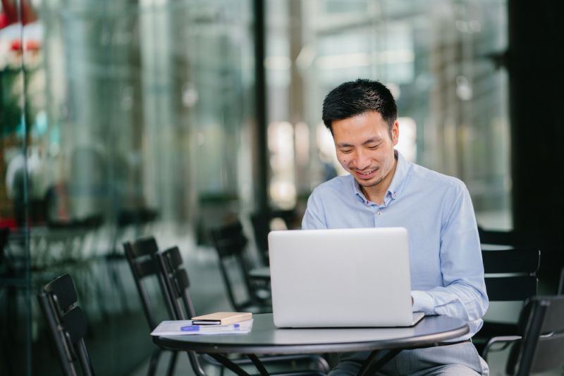 Young Asian man working on his laptop outside of a cafe